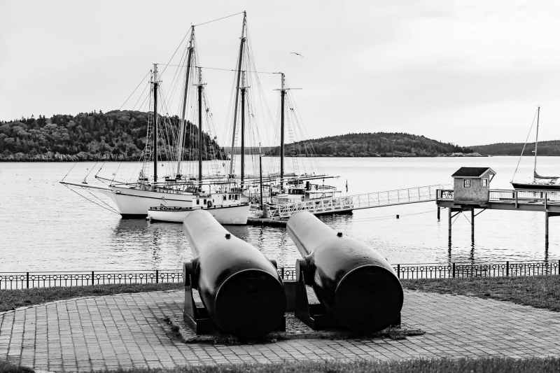 Shades of the Spanish American war: Pair of antique cannons in public square seem to point toward two schooners and a smaller boat docked nearby in Bar Harbor, Maine, USA, early morning in summer
